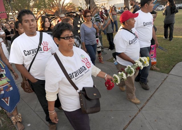 ROB VARELA/THE STAR Blanca Luz Nava Velez (second from left) and Estanislao Mendoza Chocolate, part of the Caravana 43, hold a cane covered with 43 white flowers that was made and presented to them by local dancers as they lead a march Thursday in Oxnard. Velez’s son Jorge and Chocolate’s son Miguel are among 43 students missing in Mexico. 